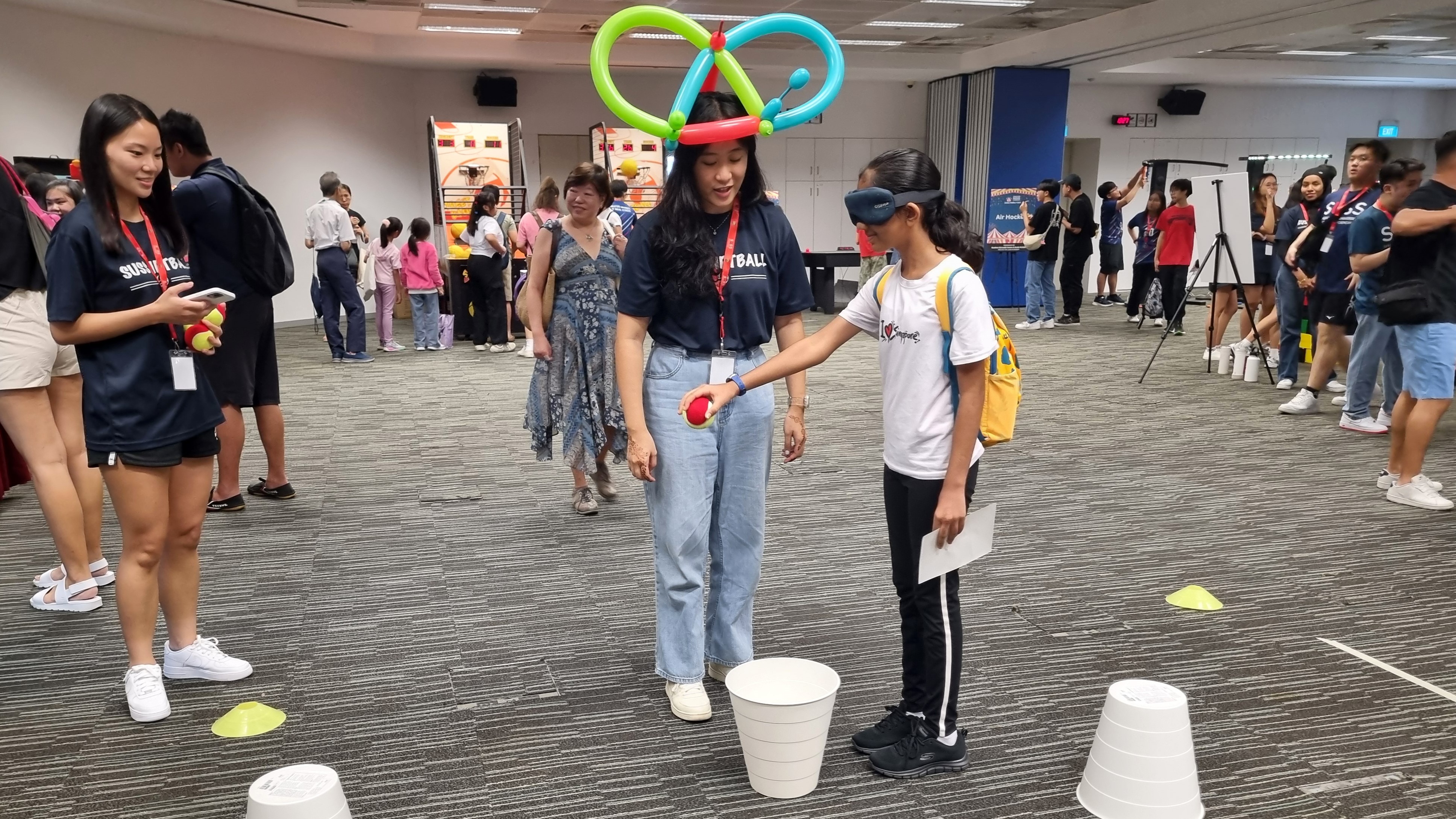 A young participant takes on an exciting blindfolded obstacle course, expertly guided by supportive volunteers, during a community bonding event.