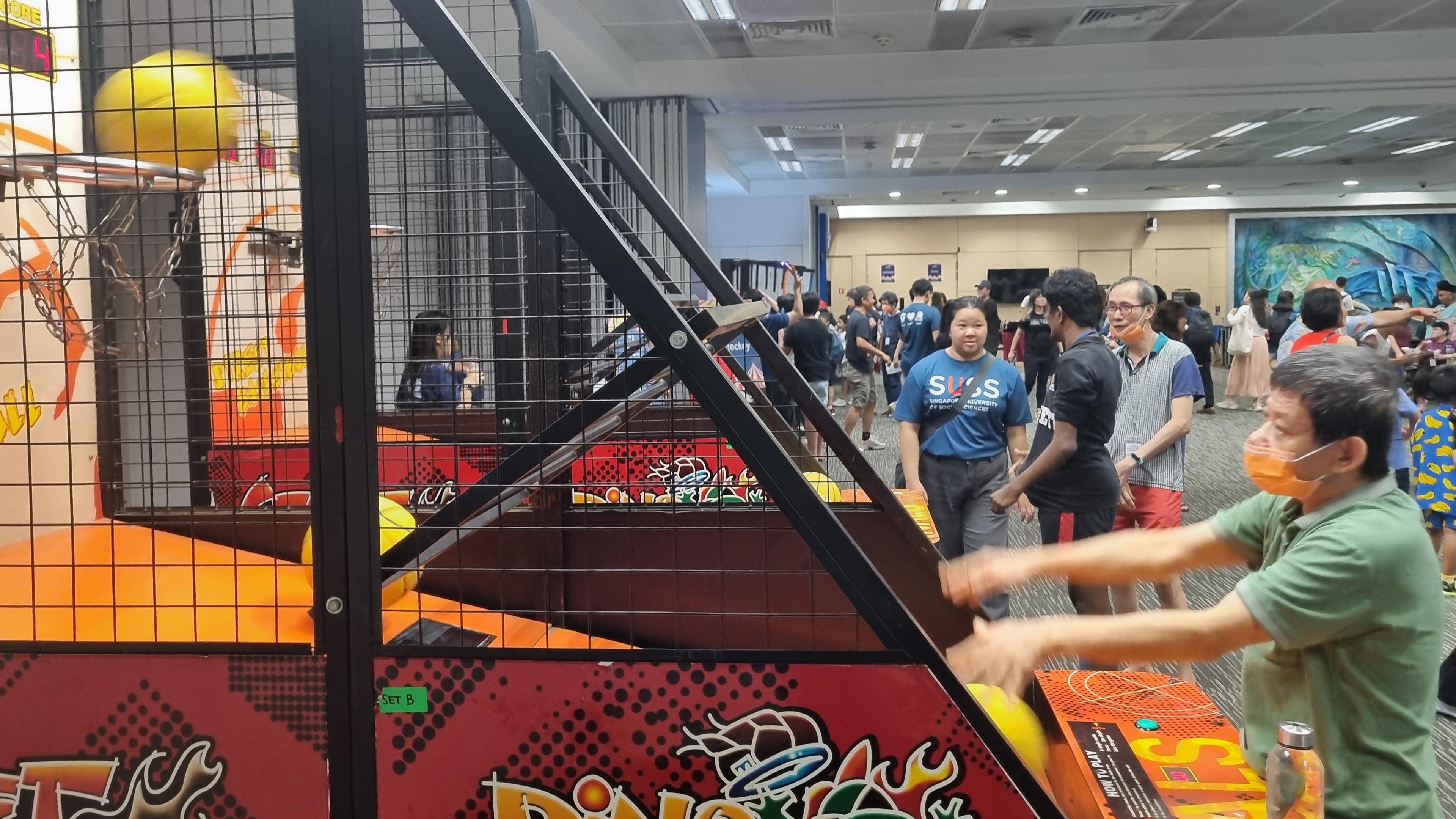 Participants of all ages enjoy a lively basketball arcade game, showcasing friendly competition and camaraderie at the community event.